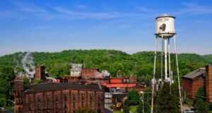 Buffalo Trace Distillery with a water tower against a backdrop of lush greenery under a blue sky.